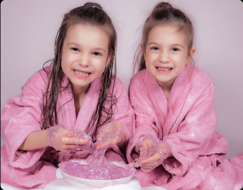 Two children in pink robes making glitter slime together