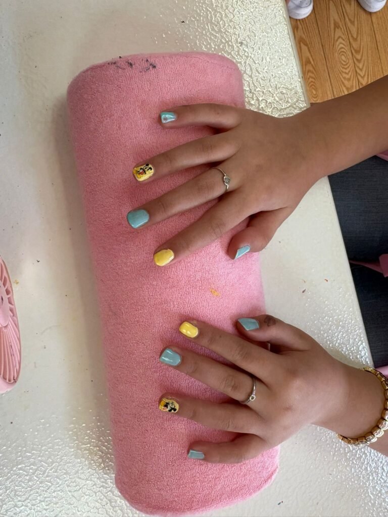 Hands with pastel blue and yellow manicured nails resting on a pink towel.
